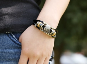 Close-up of a layered leather skull bracelet with wooden beads on a model's wrist