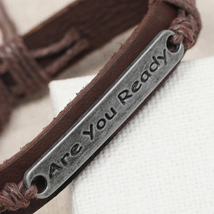 Macro shot of Are You Ready engraved vintage metal plate on braided leather bracelet
