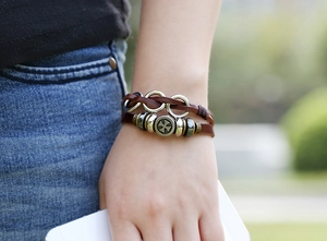 Detail of multi-layer brown leather braided bracelet with metallic cross beads on wrist