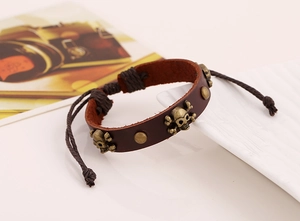 Détail d'un bracelet en cuir marron foncé avec crânes et clous sur un plateau blanc