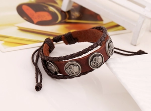 Detail eines mehrlagigen Lederarmbands mit silbernen Totenkopf-Anhängern und Flechtschnüren