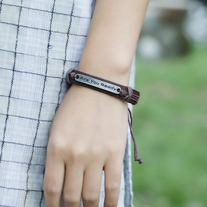 Macro detail of multilayer braided leather bracelet with Are You Ready engraved metal plate