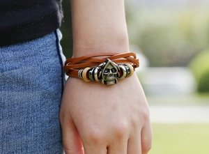Close-up of a multi-layer brown leather bracelet with an antique silver skull charm and wood beads