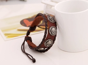 Nahaufnahme eines Punk-Lederarmbands mit Vintage-Totenkopf-Anhängern an einer weißen Tasse