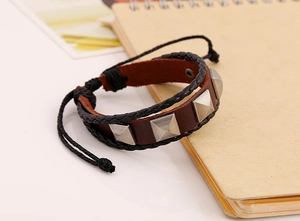 Close-up of leather bracelet with silver pyramid studs and braided cord on a notebook