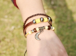 Detail of stacked leather bracelets with moon charm and beads in retro bohemian style