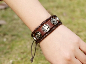 Detail eines dunkelbraunen Lederarmbandes mit drei silbernen Totenkopfnieten und Kordeln