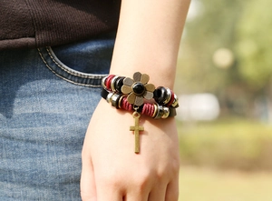 Detail of multilayer leather bracelet featuring a cross charm and vintage floral bead