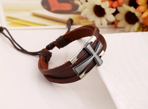 Dettaglio macro di un bracciale multistrato in pelle marrone vintage con ciondolo a croce