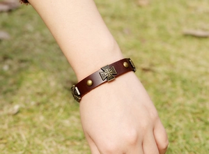 Gros plan du bracelet en cuir marron avec croix de Malte en bronze sur l'herbe