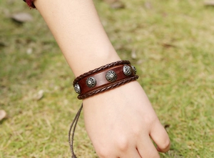 Macro shot of brown leather woven bracelet with engraved silver rivets on a green grass background