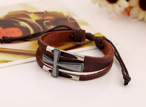 Dettaglio di bracciale in pelle marrone con croce in metallo antico e chiusura regolabile