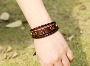 Détail d'un bracelet en cuir multicouche avec des roses en bronze sur fond d'herbe