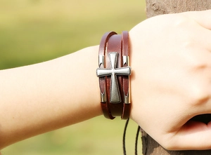 Dettaglio di un bracciale in pelle marrone multistrato con ciondolo a croce in metallo vintage