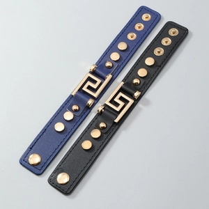 Detail of leather punk bracelets featuring gold Greek key motif and metal rivets