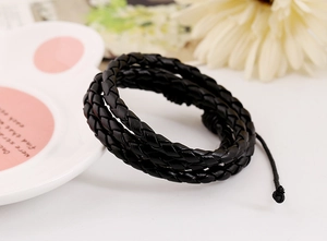 Close-up of black multi-strand braided leather bracelet with adjustable knot on plate