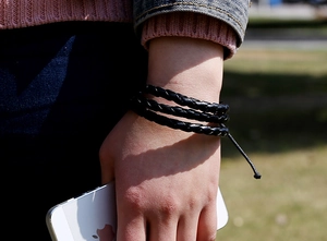 Detail of a multi-layer black braided leather wrap bracelet with adjustable cord closure