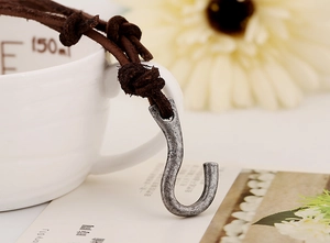 Macro view of vintage metal hook pendant with dark brown braided leather necklace strap