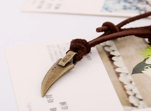 Macro shot of retro bronze fang pendant on brown leather cord with distressed metal detail
