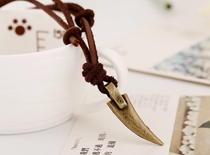 Detail view of retro bronze fang pendant and textured dark brown leather cord necklace
