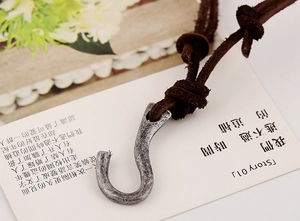 Macro detail of vintage alloy hook pendant with brown leather cord on a white card