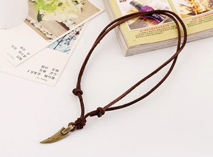 Close-up of vintage leather cord necklace with bronze wolf tooth pendant on a desk
