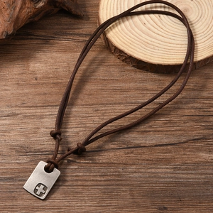 Macro shot of retro metal cross pendant with adjustable dark brown leather cord on wood