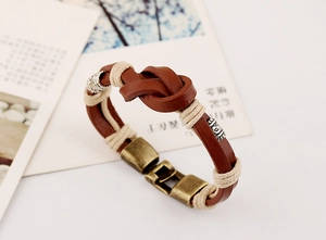 Détail d'un bracelet en cuir marron tressé avec fermoir en bronze et tubes métalliques gravés