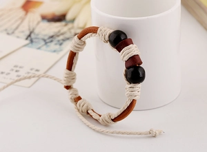 Close-up of handmade braided brown leather bracelet with white cotton cord and black beads