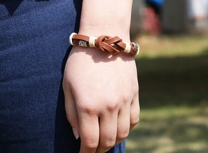 Gros plan d'un bracelet en cuir marron tressé avec des perles argentées au poignet