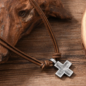 Detail of vintage woven leather necklace with aged metal cross pendant on wood
