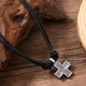 Detail view of a vintage alloy cross pendant on a black leather cord over wood