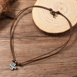 Vintage woven cross pendant on brown leather cord necklace displayed on rustic wood background