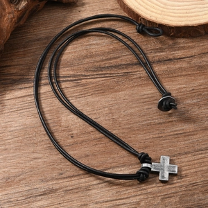 Detail of vintage metal cross pendant on black leather cord against a wood background