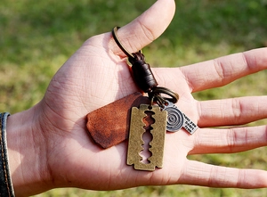 Close-up of vintage leather keychain featuring metal razor blade and engraved charms