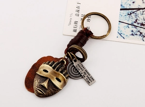 Detail of vintage bronze African mask keychain with engraved metal tag and brown leather