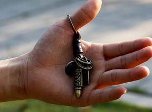 Detail of vintage braided leather keychain with bronze metallic bullet pendant