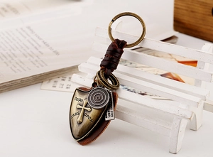 Detail of vintage woven leather keychain with brass shield cross and metal tags