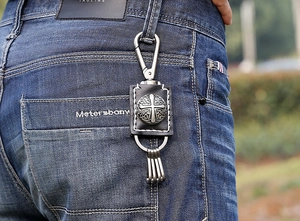 Retro leather keychain with cross emblem hanging on blue jeans waist belt loop