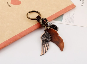 Détail d'un porte-clés aile vintage avec plumes en alliage et cuir marron sur un carnet