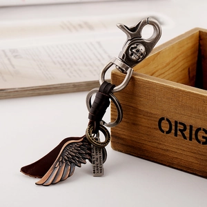 Vintage bronze wing leather keychain with skull carabiner on a rustic wooden box