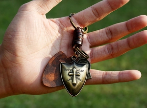 Close-up of vintage bronze shield keychain with cross relief and woven leather strap