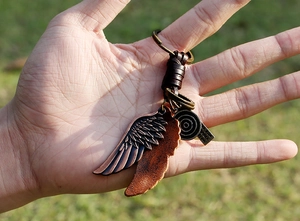 Détail du porte-clés en cuir vintage avec ailes en bronze, corde tressée et médailles