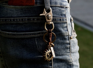 Close-up of vintage punk leather keychain with skull hook hanging on denim jeans