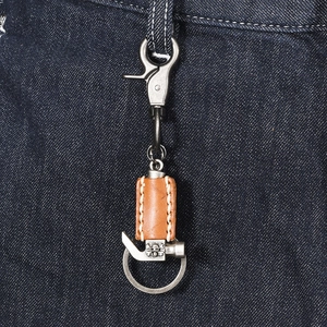 Handmade leather keychain with punk hammer pendant on denim background texture