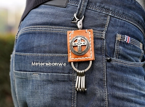 Detail of vintage brown leather keychain with metal cross relief on denim jeans pocket