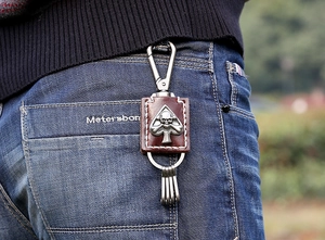 Detail of punk leather keychain with metal skull relief hanging on denim jeans