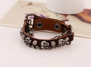 Detail view of dark brown leather punk bracelet featuring skull studs and metal chains