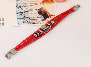 Détail d'un bracelet punk en cuir tressé rouge avec crâne et os croisés en métal vintage
