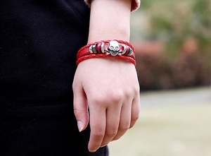 Détail d'un bracelet en cuir tressé rouge avec un charm tête de mort punk en argent